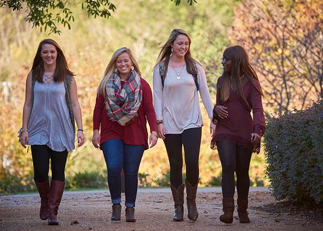 {Four female students walk towards the camera on an autumn day}